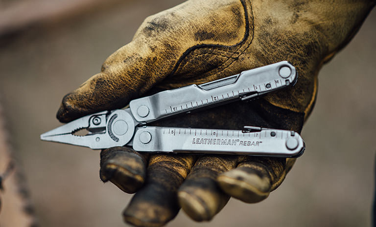 Man with dirty yellow leather gloves holding Leatherman Rebar