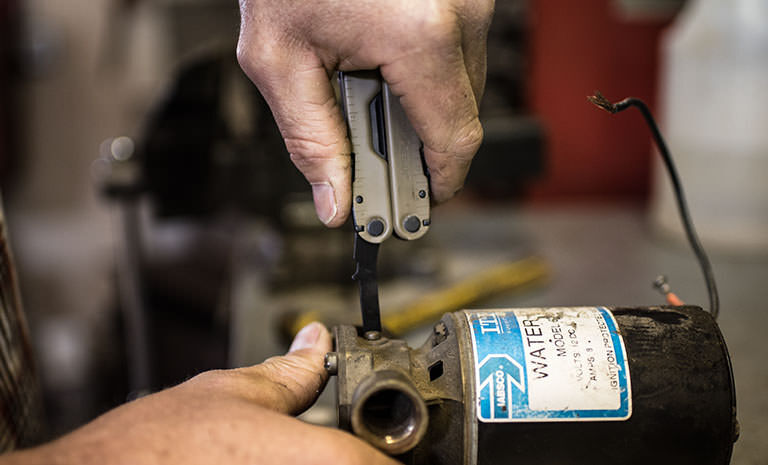 Man using Leatherman Rebar flat head screwdriver to screw on tank